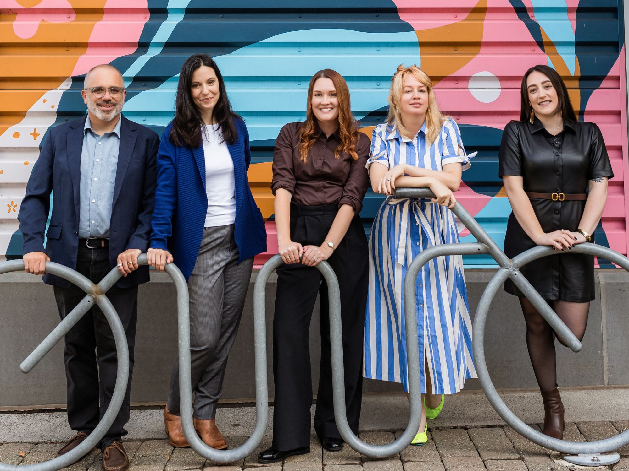 The five-person Best Era team leaning on a metal sculpture in front of a bright floral mural